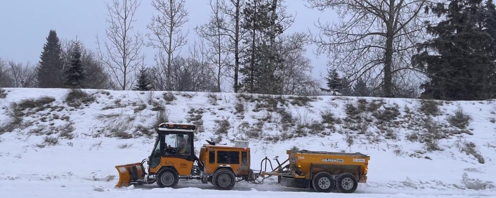 Small plow with trailer clearing snow from pathway in winter.